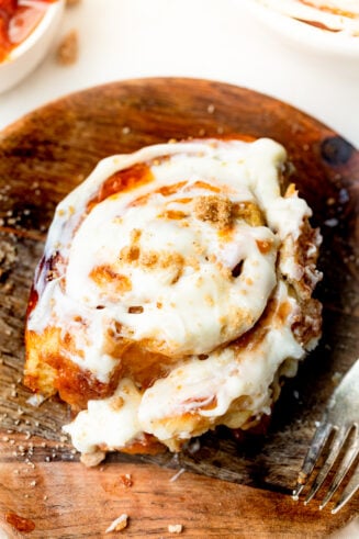 a photo of a peach cinnamon rolls sitting on a wooden dessert plate loaded with peach jam and topped with peach cream cheese frosting