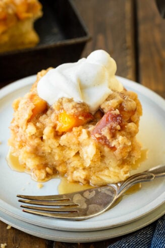 a photo of a serving of golden baked peach cobbler french toast casserole topped with a dollop of whipped cream