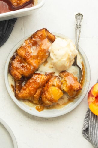 three golden baked peach dumplings with a scoop of vanilla ice cream melting on top and a spoon scooping into one of the dumplings