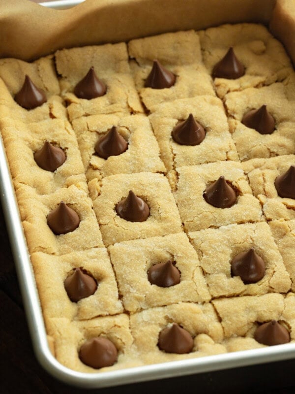a baking pan of baked peanut butter blossom bars each topped with a melty hersheys kiss