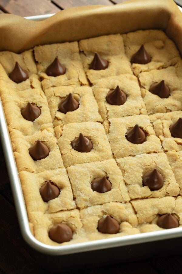 a baking pan of baked peanut butter blossom bars each topped with a melty hersheys kiss