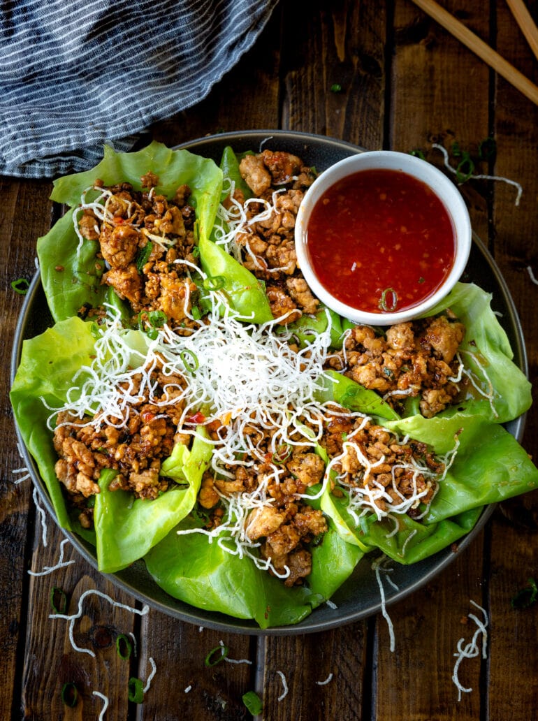 a photo of a large platter full of several Asian chicken lettuce wraps and a small bowl of a sweet chili dipping sauce.