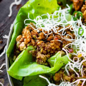 a photo of a chicken lettuce wrap topped with crispy rice noodles.