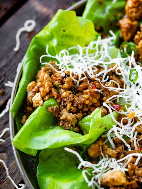 a photo of a chicken lettuce wrap topped with crispy rice noodles.