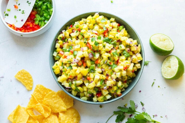 a large bowl of fresh pineapple salsa with tortilla chips sitting next to it and a fresh lime halved.