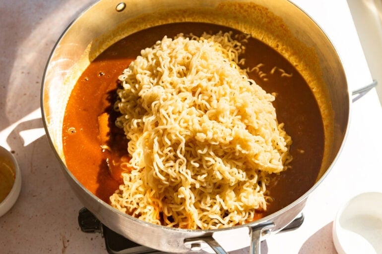 cooked ramen noodles sitting in peanut butter sauce in a pan ready to be stirred together