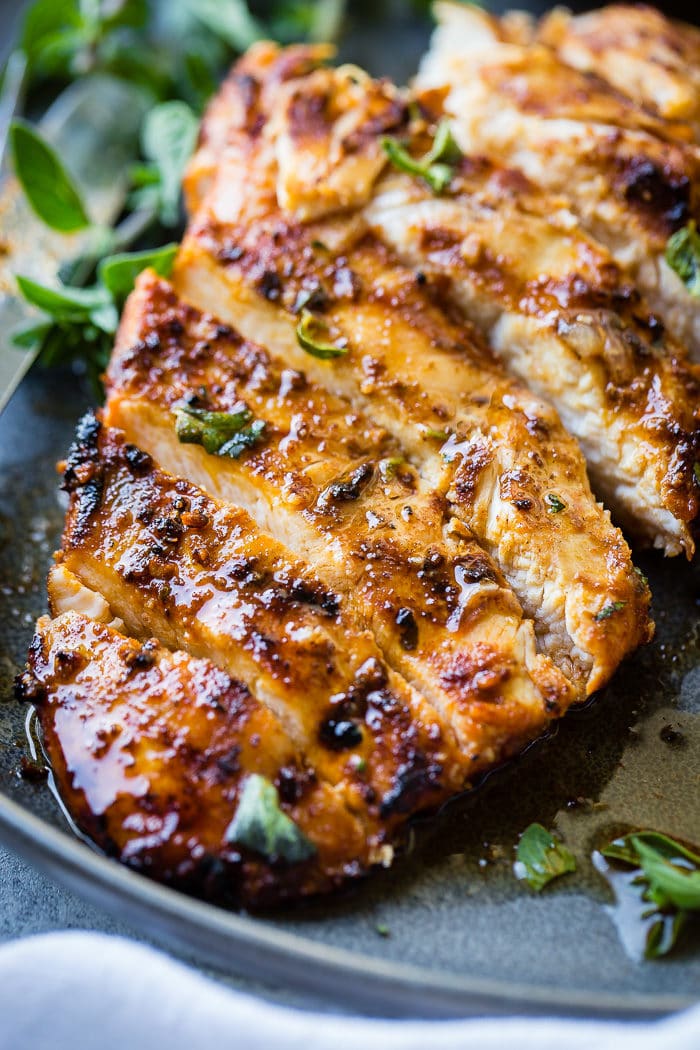 A grey plate with a sliced quick grilled chicken with oregano with oregano and grilled lemons behind it