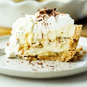 a photo of a large slice of double layered banana pudding pie topped with whipped cream and shaved chocolate