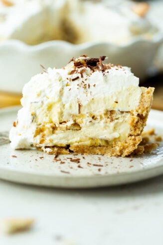 a photo of a large slice of double layered banana pudding pie topped with whipped cream and shaved chocolate