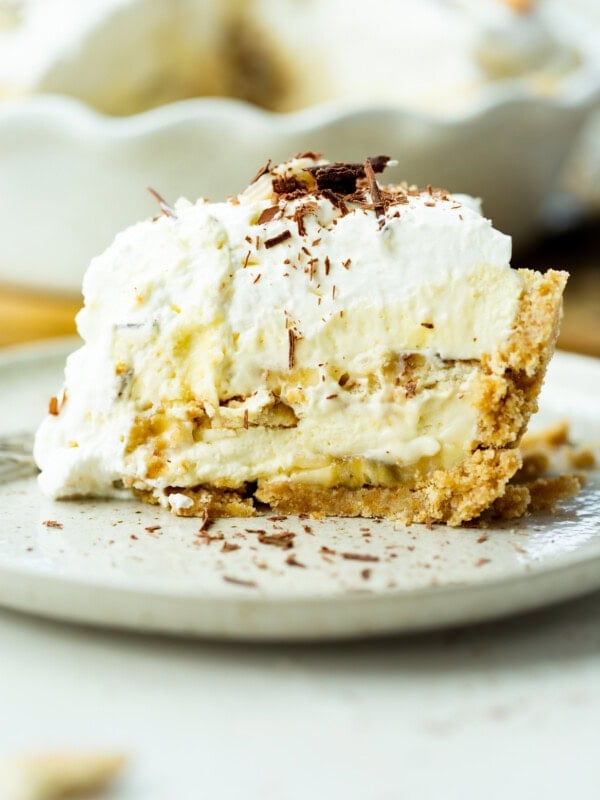 a photo of a large slice of double layered banana pudding pie topped with whipped cream and shaved chocolate