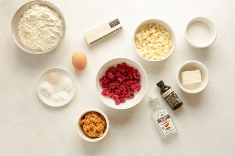 all the ingredients for white chocolate raspberry cookies in separate small bowls sitting on a white table