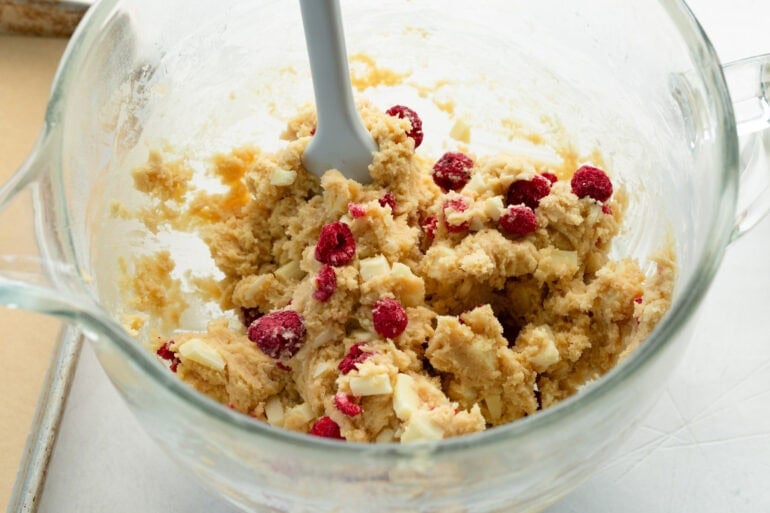 a large glass bowl with white chocolate raspberry cookie dough being stirred by a wooden spoon