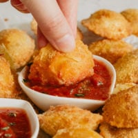 a plate full of easy fried ravioli with one being dipped in marinara sauce
