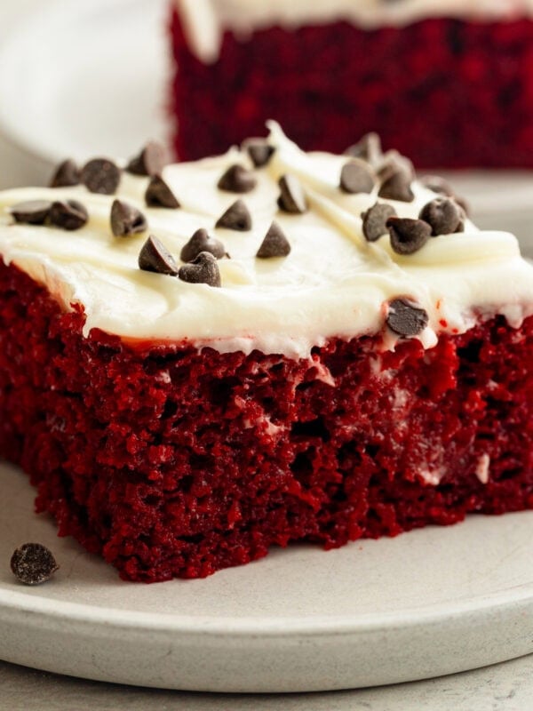 a piece of moist red velvet cake topped with white cream cheese frosting and sprinkled with mini chocolate chips