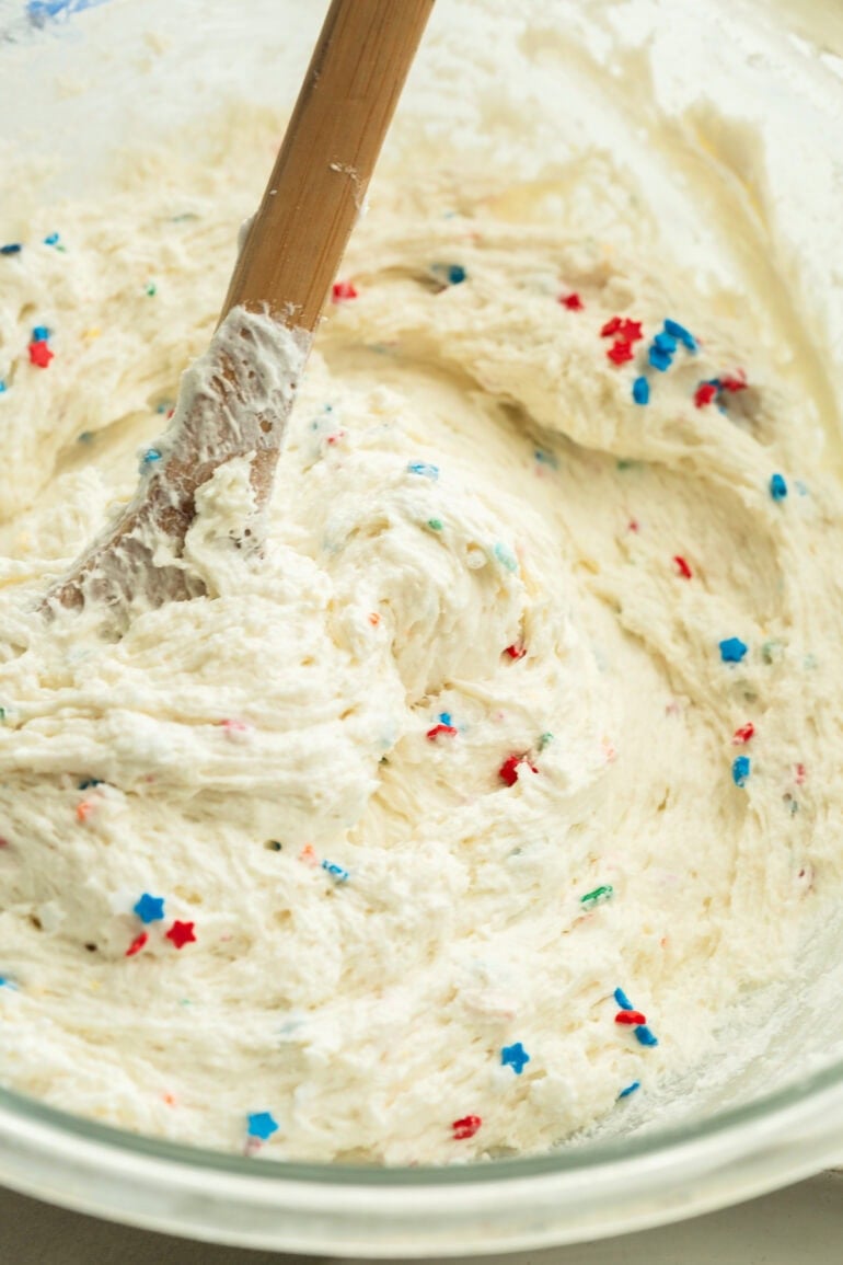 A close up photo of a glass bowl filled with creamy dessert cream topped with red white and blue sprinkles.