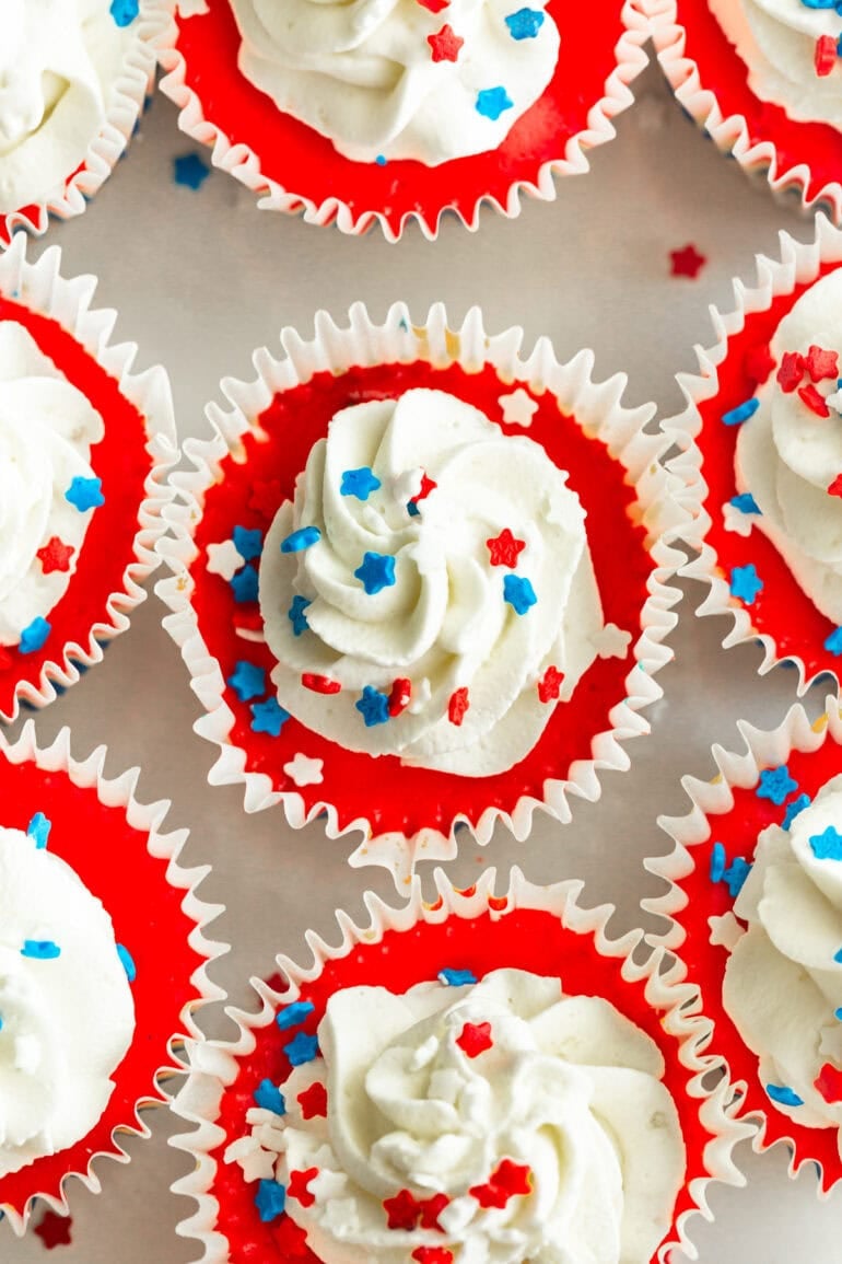 an overhead shot of a plate full of layered red, white, and blue cheesecakes with a swirl of whipped cream and patriotic star sprinkles