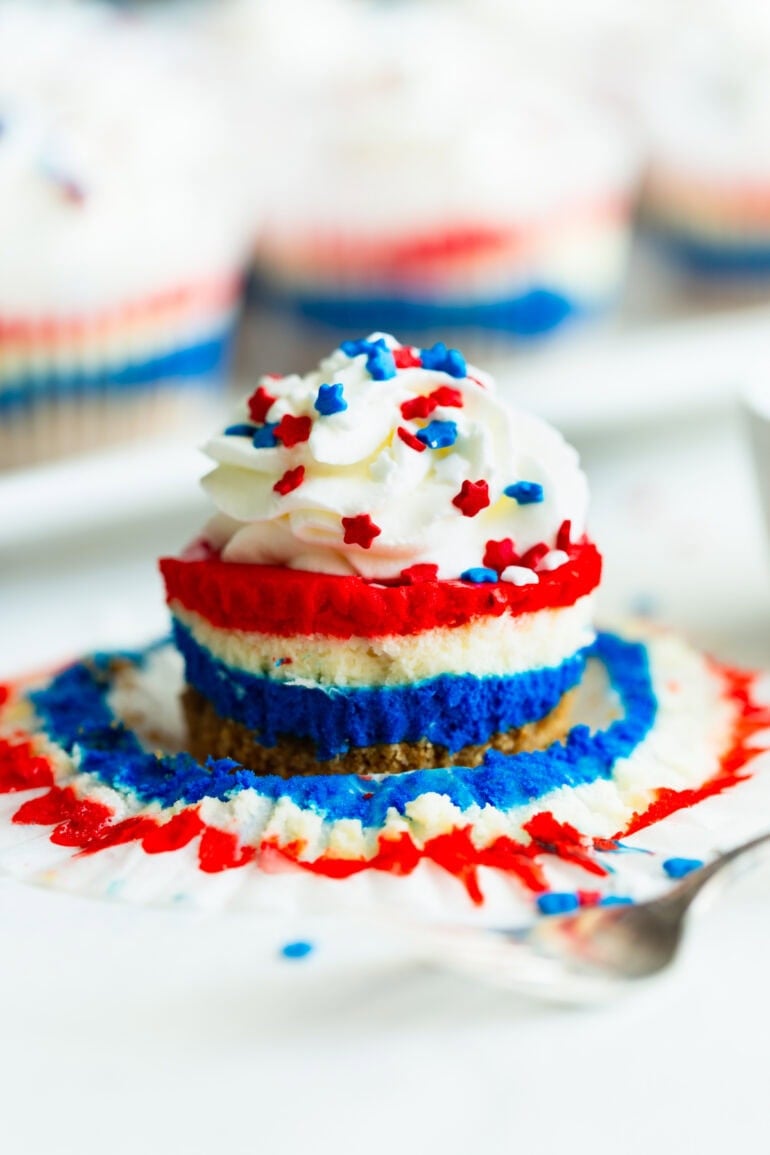 a side view of layered red, white, and blue cheese cakes with a swirl of whipped cream and patriotic star sprinkles