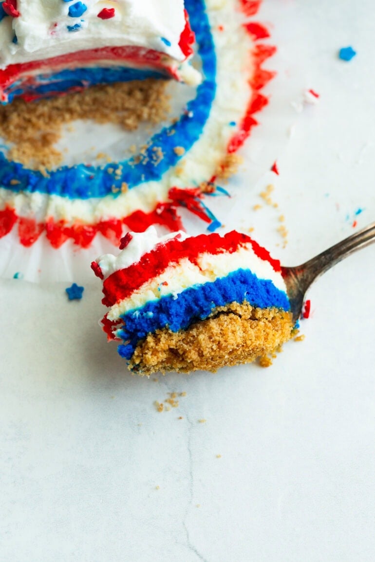 a fork with a bite of layered red, white, and blue cheesecakes with a swirl of whipped cream and patriotic star sprinkles