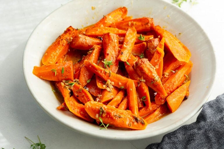 buttery tender carrots topped with fresh thyme in a large white serving bowl