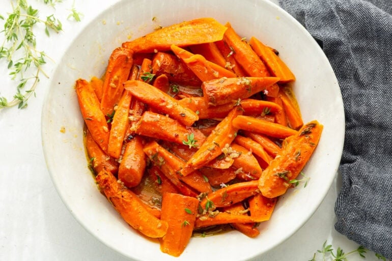 a large white serving bowl of sliced, tender carrots topped with fresh herbs in a large white serving bowl