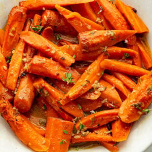 a large white serving bowl full of roasted tender carrots topped with fresh herbs