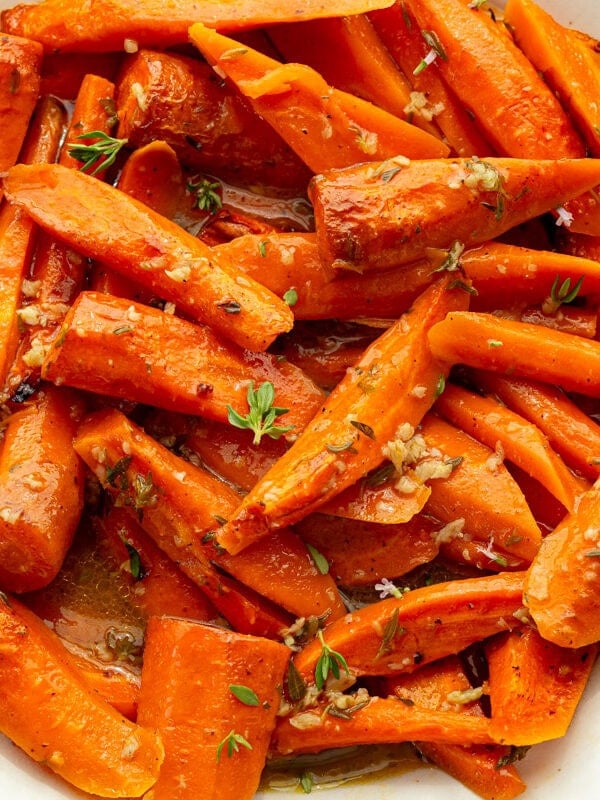 a large white serving bowl full of roasted tender carrots topped with fresh herbs