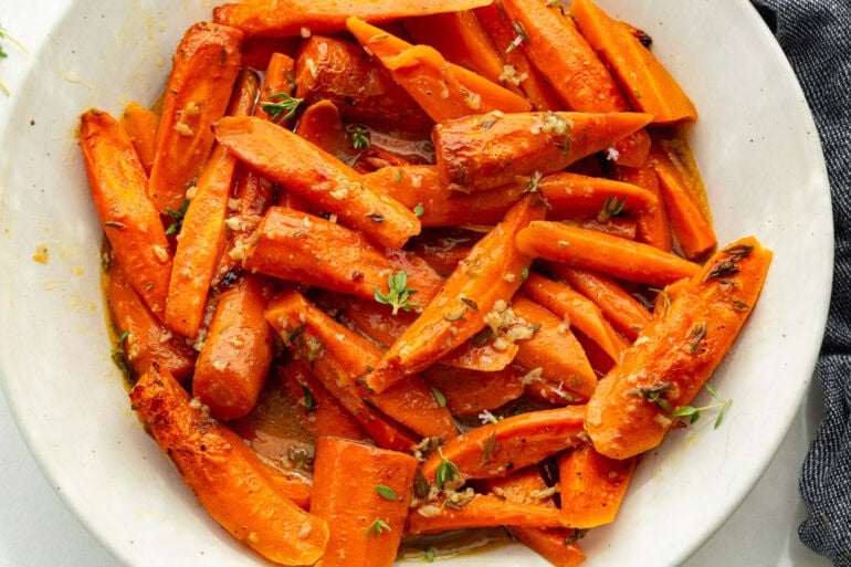 a large white serving bowl full of roasted  tender carrots topped with fresh herbs
