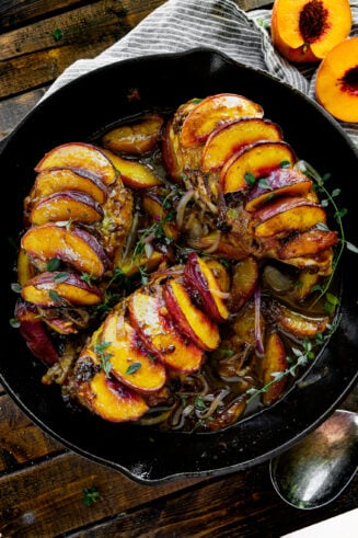 a photo of a large cast iron skillet with three chicken breasts in it each covered in sliced peaches