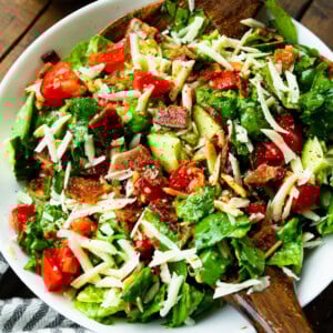 a photo of a large bowl full of a green salad with slivered almonds, tomatoes, and bacon crumbles