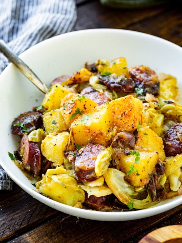 a photo of a large white bowl filled with braised sausage cabbage and potatoes ready to be served for dinner.