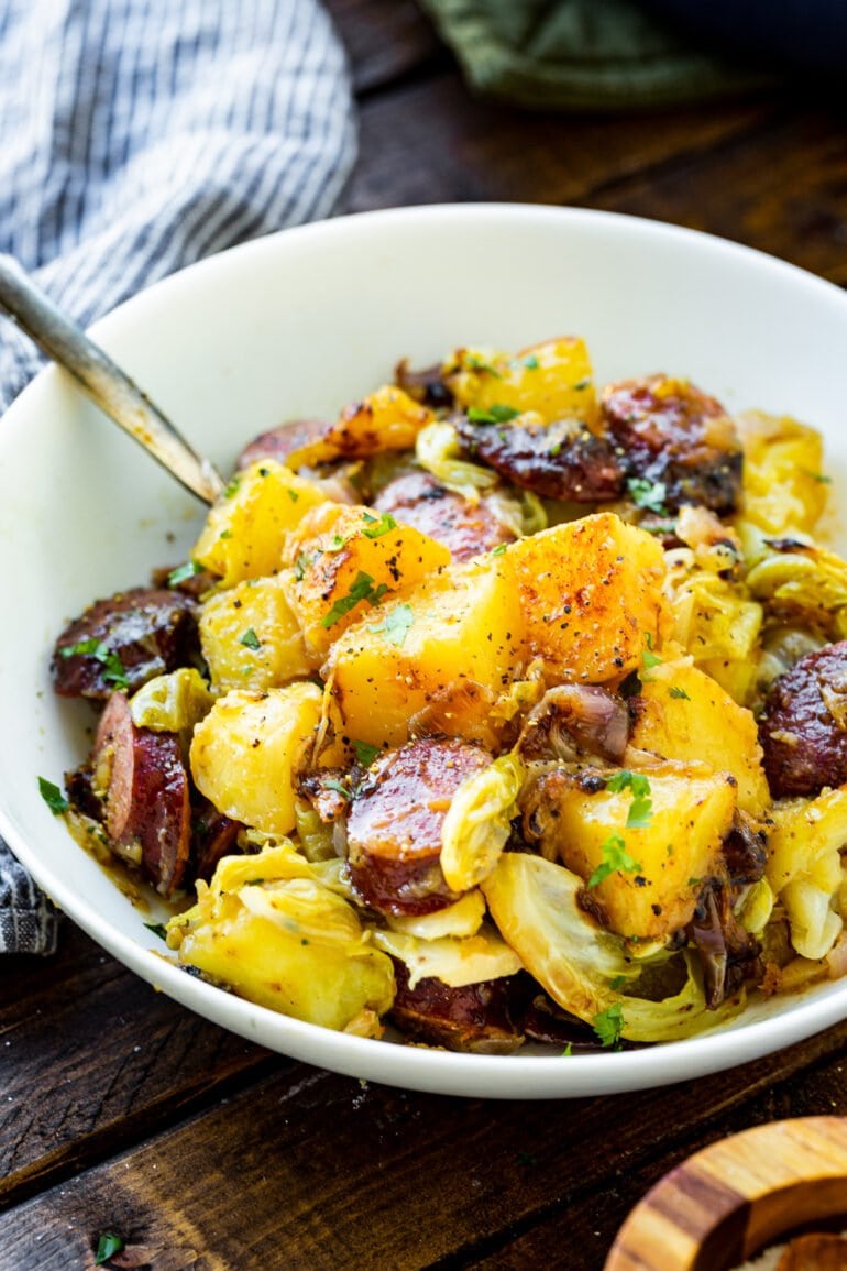 a photo of a large white bowl filled with braised sausage cabbage and potatoes ready to be served for dinner.