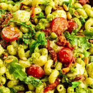 a large bowl of creamy pesto pasta with halved cherry tomatoes, arugula and sun dried tomatoes