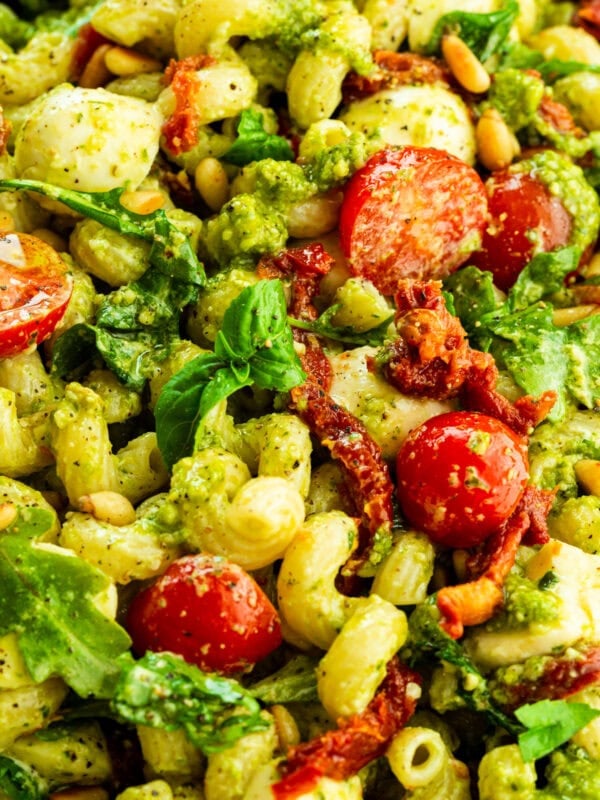 a large bowl of creamy pesto pasta with halved cherry tomatoes, arugula and sun dried tomatoes