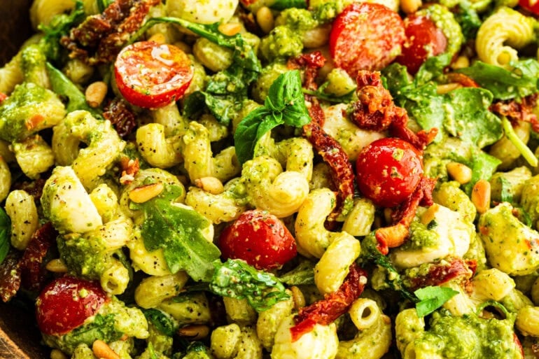 creamy pesto pasta salad made with spiral pasta with arugula, cherry tomatoes, mozzarella balls, and pine nuts