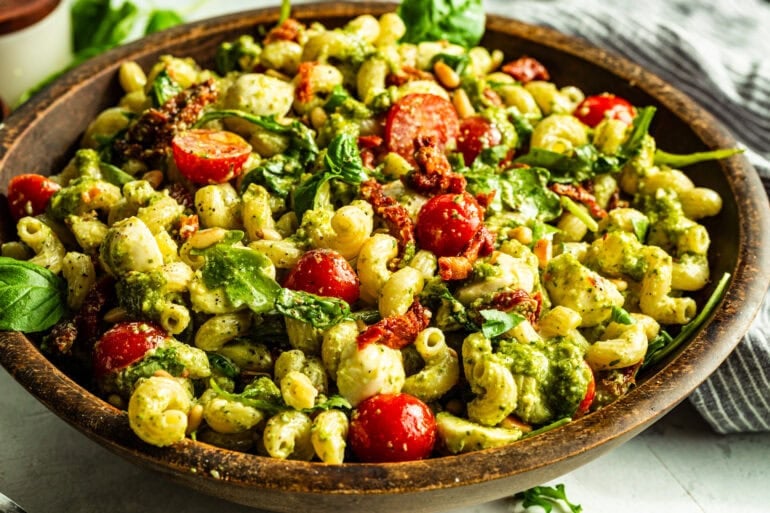 a large wooden serving bowl full of pesto pasta salad