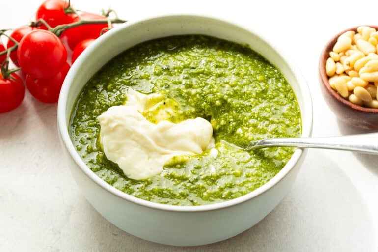 a large bowl of fresh homemade pesto with a dollop of mayonnaise about to be stirred together