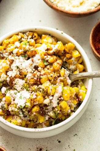 a photo of a white serving bowl full of roasted sheet pan mexican street corn topped with cotija cheese