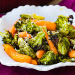 a white bowl with simple roasted garlic veggies including carrots, brussels sprouts and broccoli with a little parmesan cheese