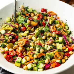 a large white serving bowl full of chickpea salad with a serving spoon in the bowl