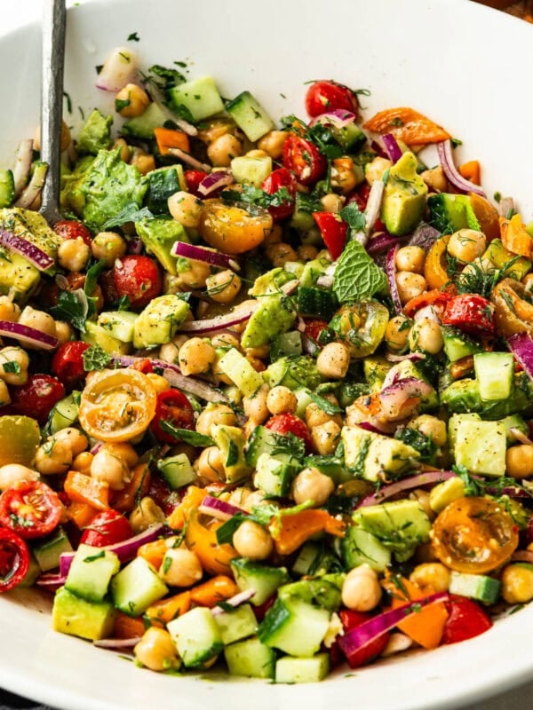 a large white serving bowl full of chickpea salad with a serving spoon in the bowl