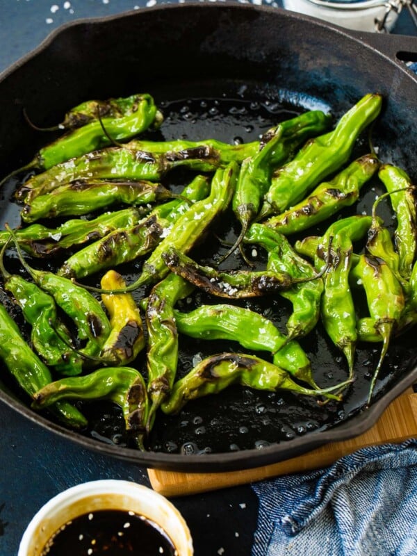 a black cast iron pan with bright green blistered shishito peppers and flaked sea salt