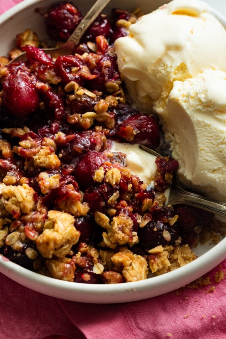 someone scooping up a bit of cherry crisp with vanilla ice cream on the side