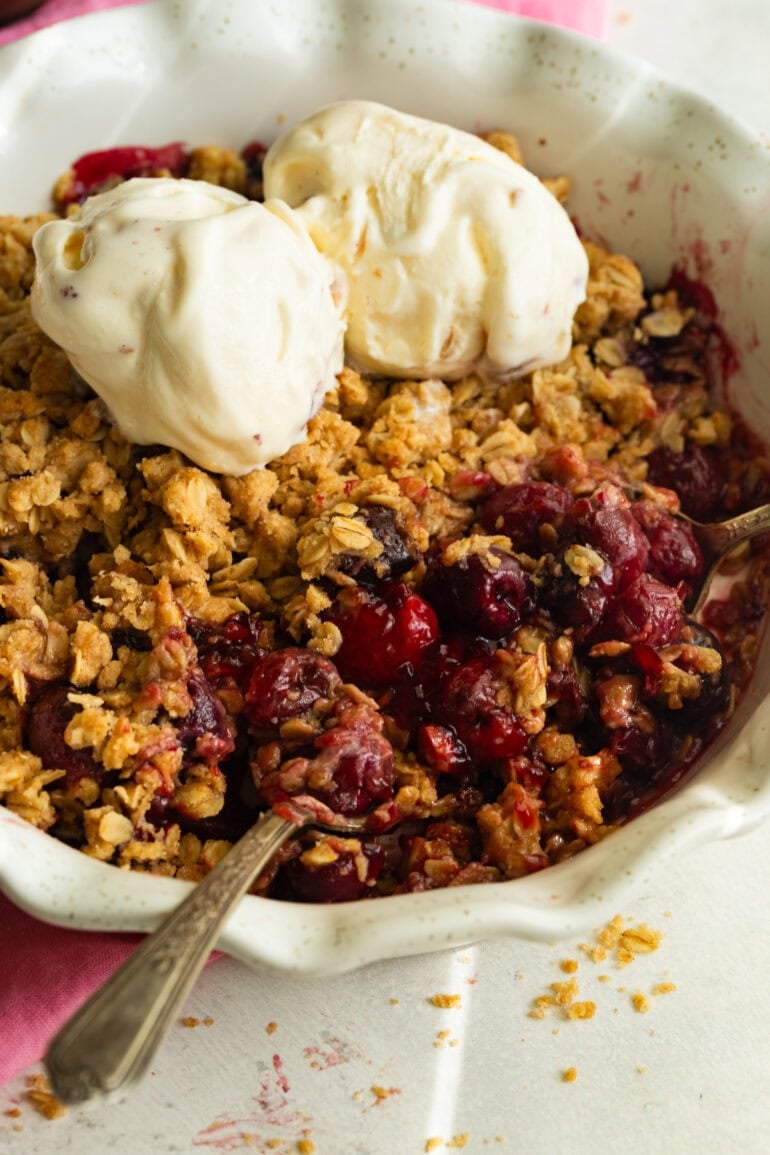 someone scooping up a bite of cherry crisp topped with scoops of vanilla ice cream