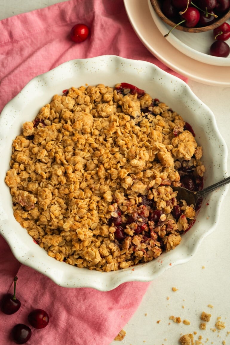 a circular white baking dish full of baked cherry crisp topped with golden oat topping