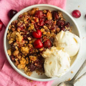 a serving of cherry crisp with oatmeal topping and two scoop of vanilla ice cream on the side