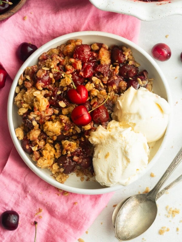 a serving of cherry crisp with oatmeal topping and two scoop of vanilla ice cream on the side