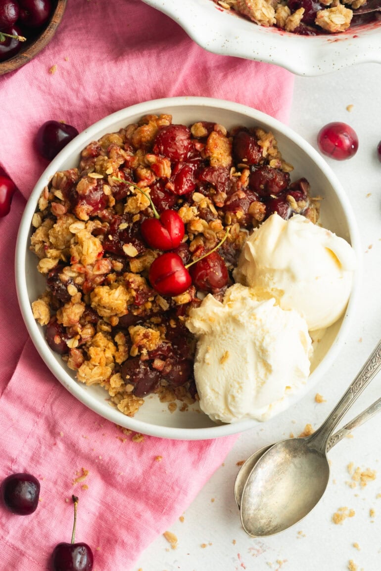 a serving of cherry crisp with oatmeal topping and two scoop of vanilla ice cream on the side