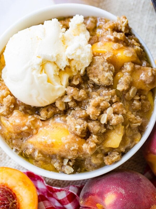 A photo of a bowl of peach crisp with a scoop of vanilla ice cream on top.