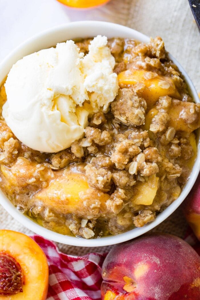 A photo of a bowl of peach crisp with a scoop of vanilla ice cream on top.