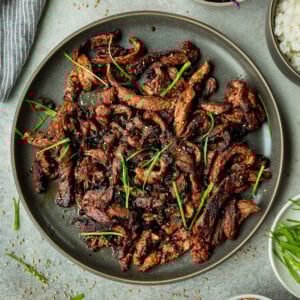 a plate of tender marinated beef strips sprinkled with sesame seeds and fresh chives